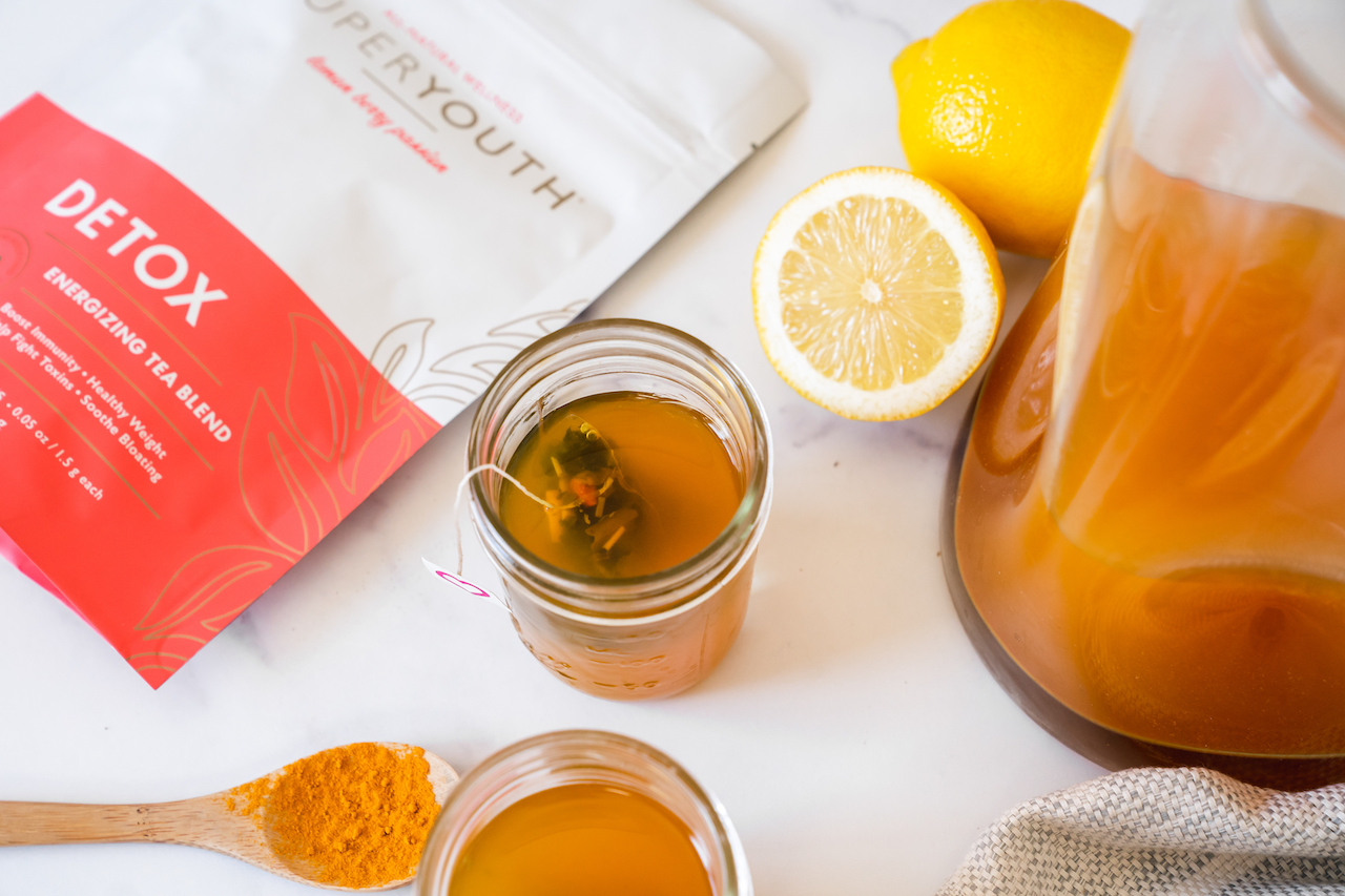 Super Youth Apple Cider Vinegar Detox tea in a glass and with a full pitcher, beside a bag of Super Youth Detox 