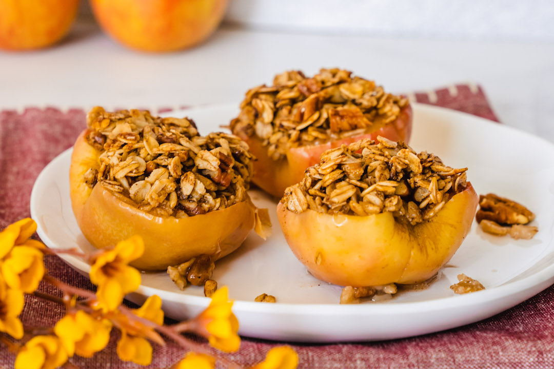 Three baked cinnamon apples with Super Youth collagen peptides on a white plate with decorative yellow flowers in the foreground.