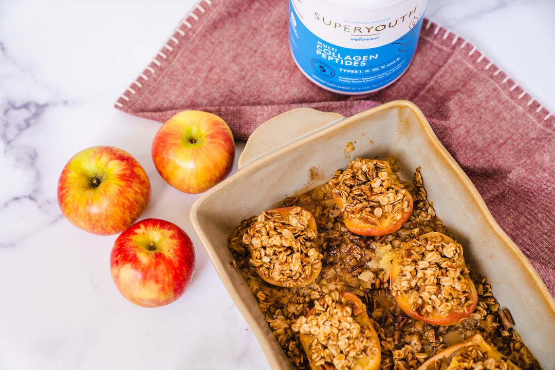 Baked Cinnamon Apples in a baking tray aside fresh apples and a Super Youth Unflavored collagen peptides.