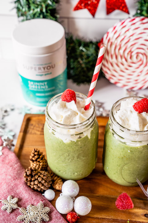 Two green Grinch Smoothies with Skinny Greens superfood powder and container in background.