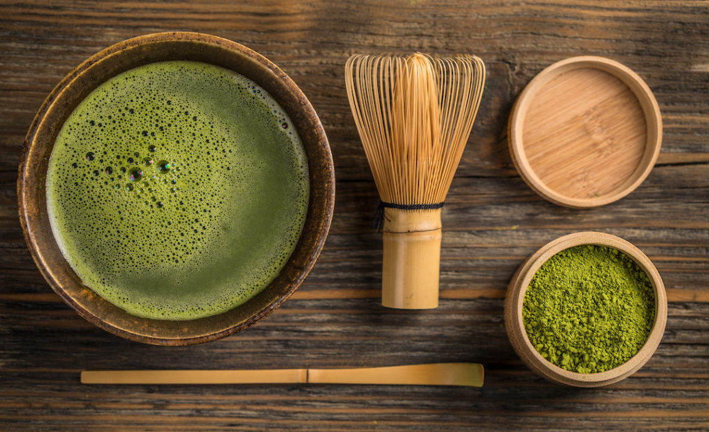 A bowl of matcha, one of the best superfoods for weight loss, with powder and mixing utensils. It's a great choice to pair with Super Youth Skinny Greens.